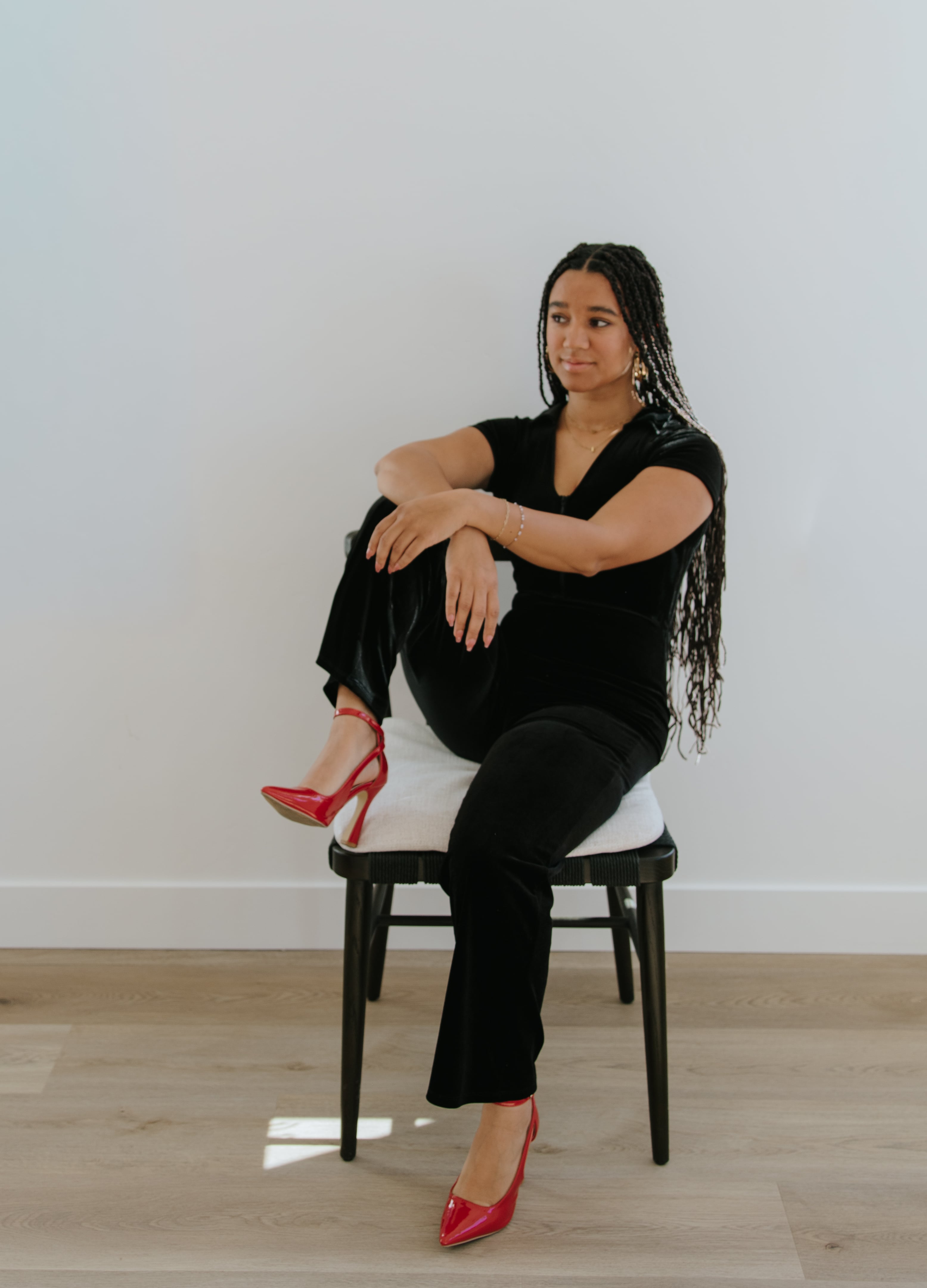 Founder seated in a black outfit with bold red shoes.
